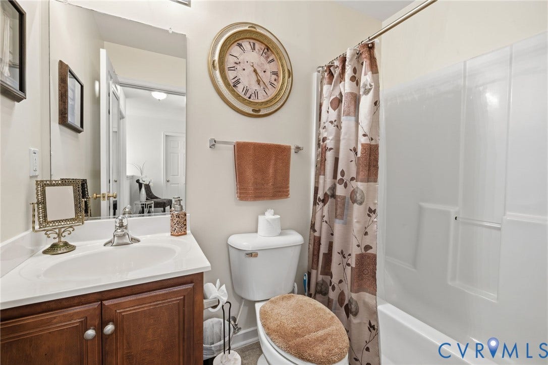 621 Scotter Hills Court, Midlothian, VA 23114 Bathroom featuring a wood-finish vanity with a white countertop and integrated sink, a large wall-mounted mirror, and a full-height acrylic tub and shower surround
