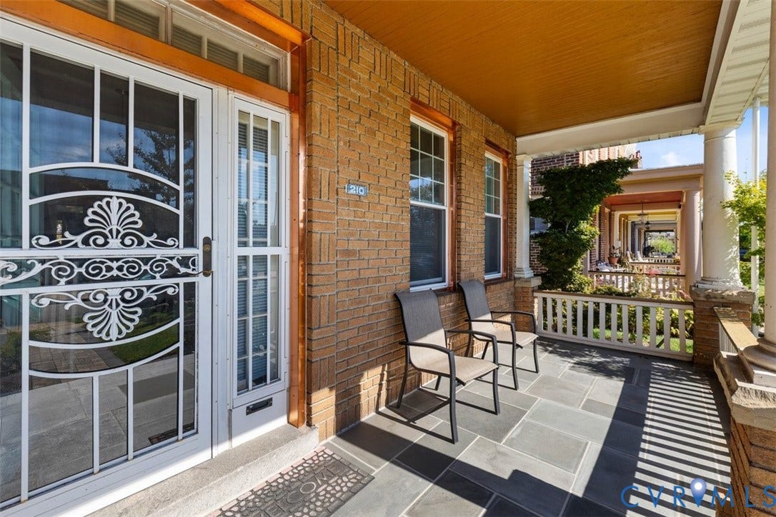 210 W Graham Road, Richmond, VA 23222 Covered front porch featuring a stone tile floor, brick exterior wall, decorative metal security door, and classic columns