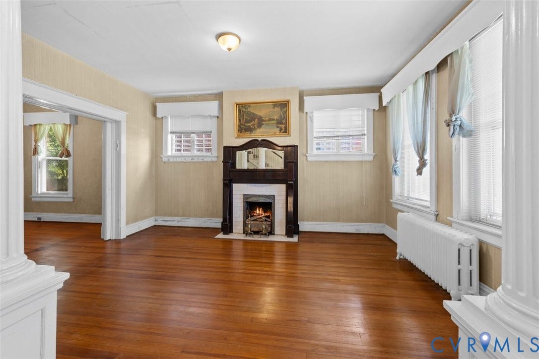 210 W Graham Road, Richmond, VA 23222 Living area featuring original wood flooring, a central fireplace with an ornate dark wood mantel, decorative column accents, and multiple windows with white trim