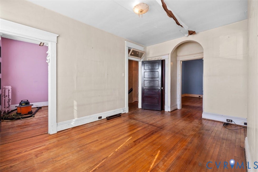 210 W Graham Road, Richmond, VA 23222 Primary bedroom featuring wood-finish flooring, historic wood-paneled door, arched doorway, and classic millwork trim