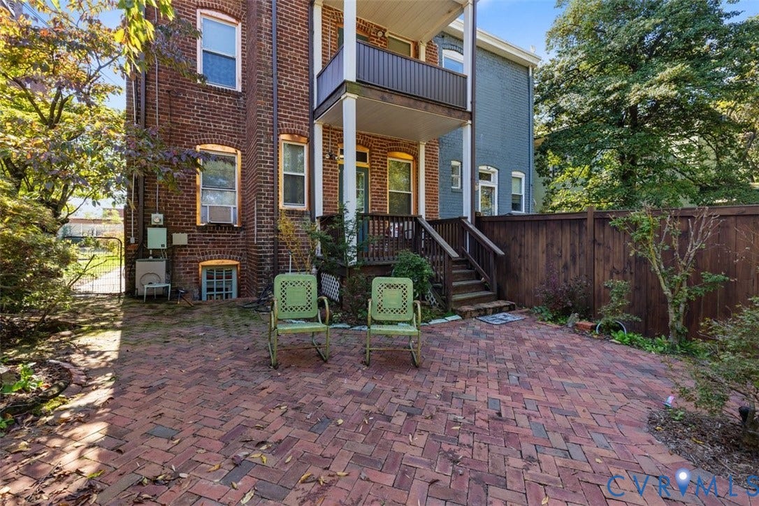 210 W Graham Road, Richmond, VA 23222 Herringbone-pattern brick patio featuring an elevated wooden deck, wood privacy fencing, and a red brick exterior facade