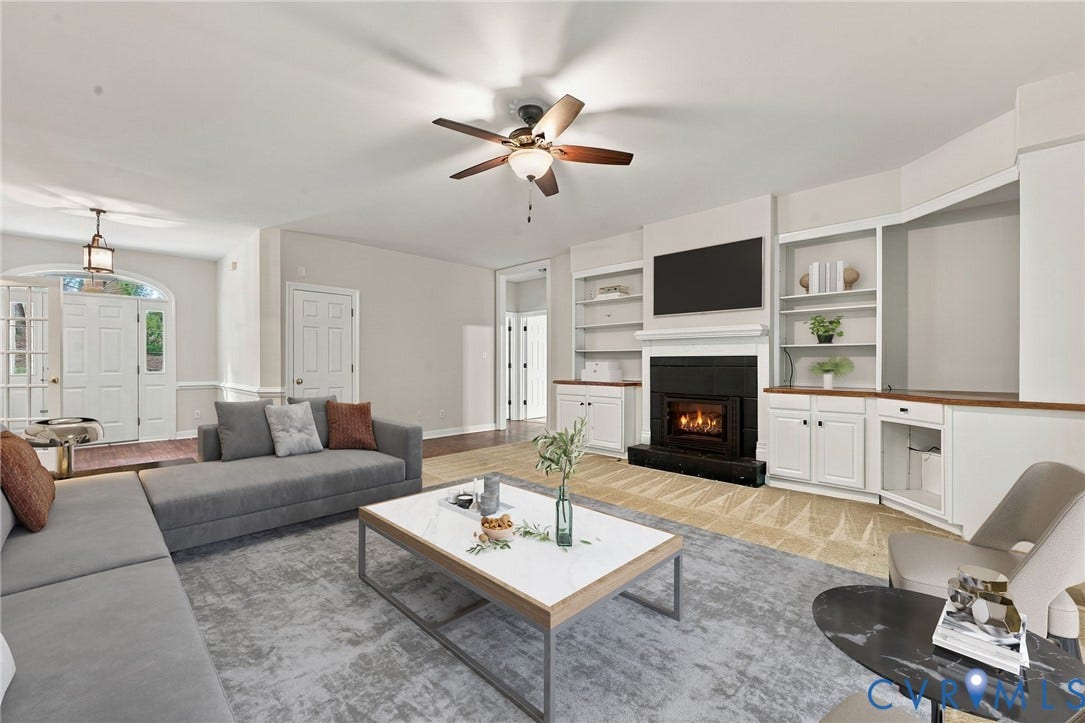 2654 Academy Road, Powhatan, VA 23139 Living area featuring a fireplace with black brick, built-in cabinetry with shelving, a ceiling fan, and a front entry door with a glass transom. Virtually staged concept