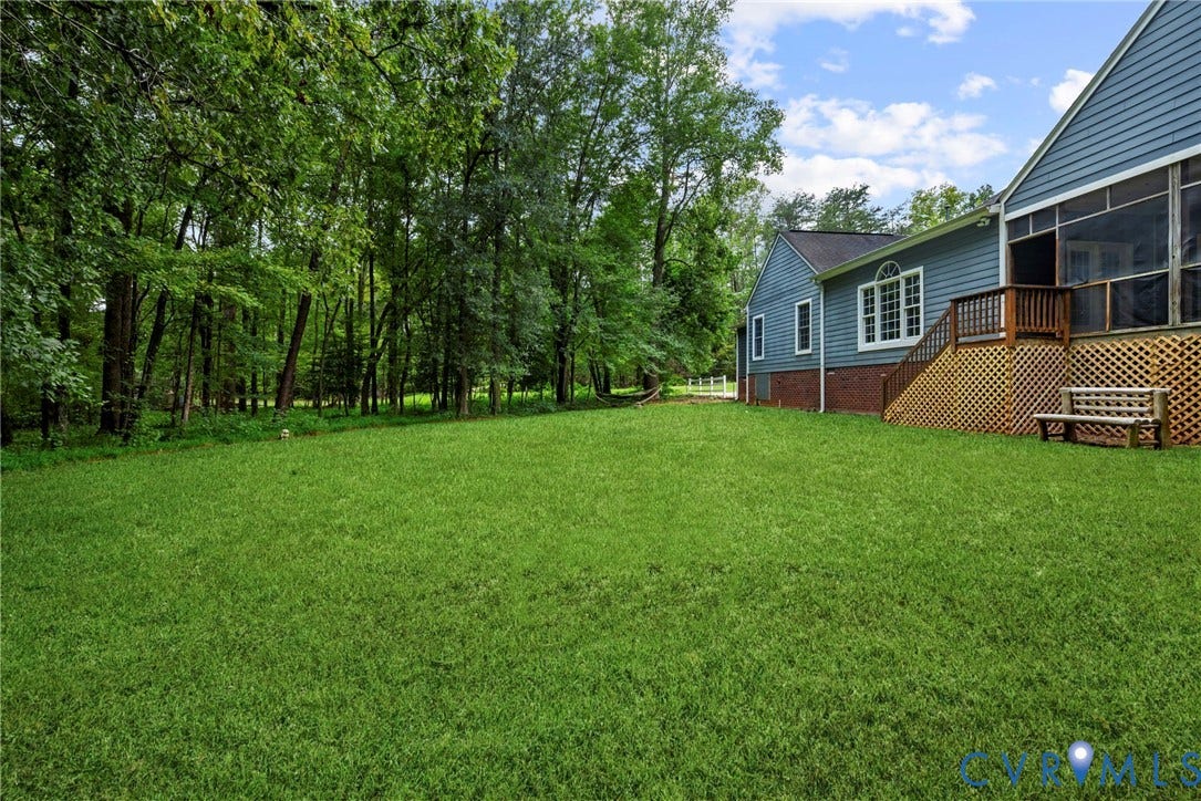2654 Academy Road, Powhatan, VA 23139 Expansive backyard featuring a level lawn, mature trees, blue-toned siding, brick foundation, and an elevated screened porch. Virtually edited grass