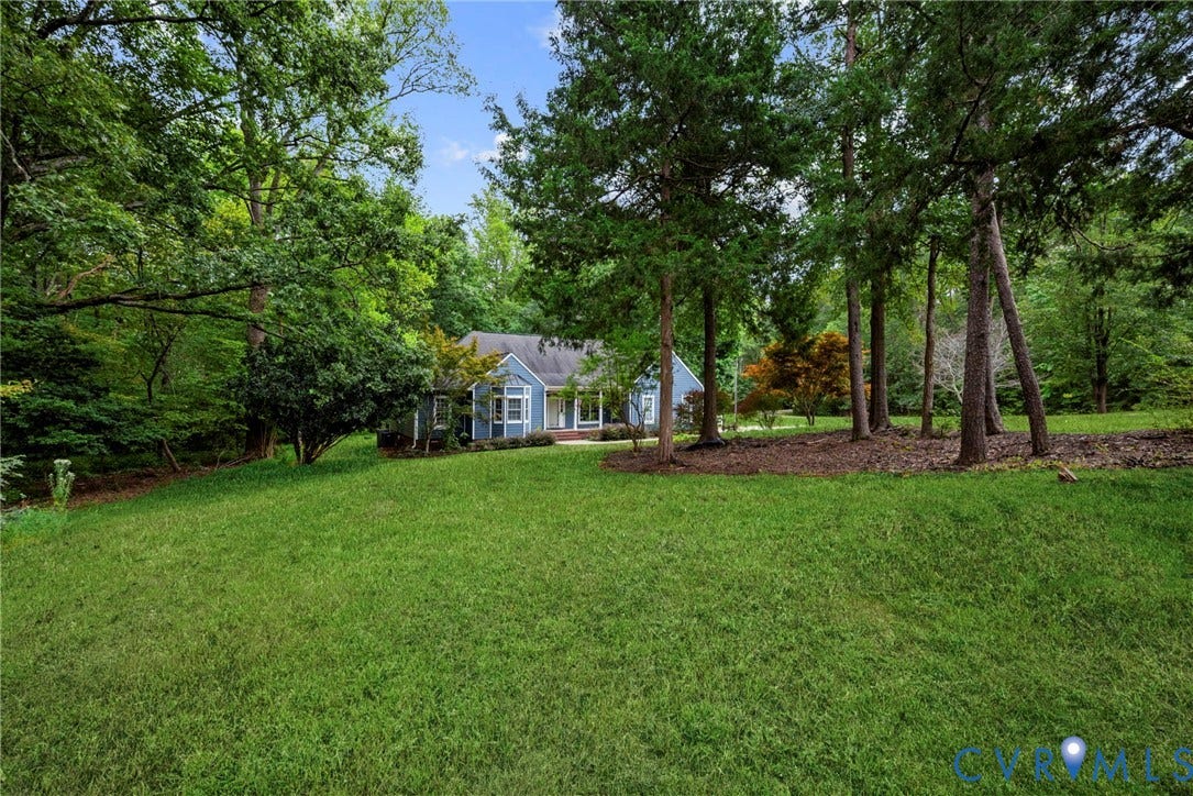 2654 Academy Road, Powhatan, VA 23139 Expansive yard featuring mature trees, wooded perimeter, and a blue-siding residence with a multi-gabled roofline. Virtually edited grass