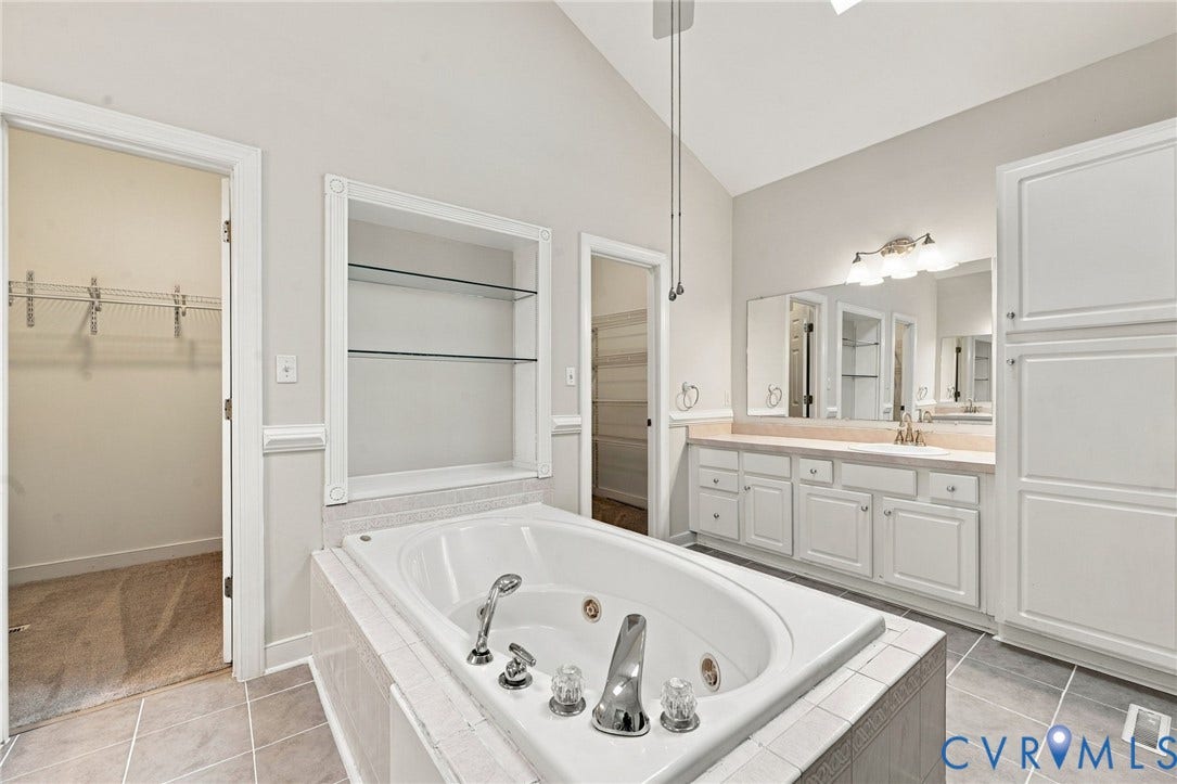 2654 Academy Road, Powhatan, VA 23139 Soaking tub with integrated jets, vaulted ceiling, built-in recessed shelving, dual-sink vanity with white cabinetry, and tall linen storage cabinet