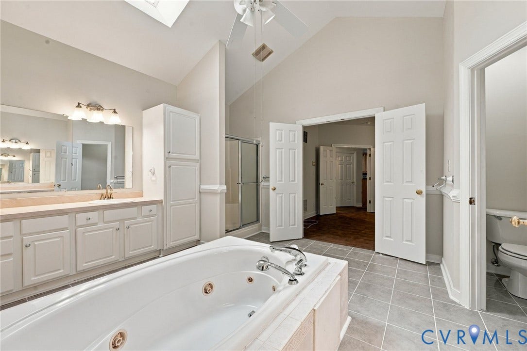 2654 Academy Road, Powhatan, VA 23139 Vaulted ceiling with skylight, jetted soaking tub, white cabinetry, tiled flooring, and built-in vanity lighting