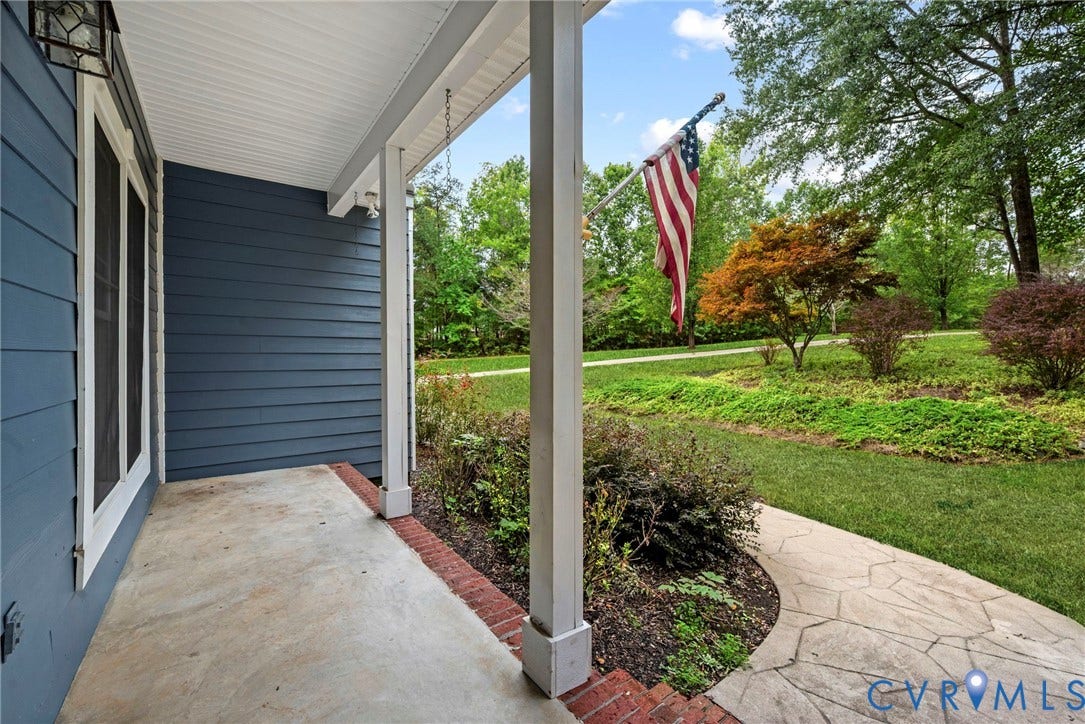 2654 Academy Road, Powhatan, VA 23139 Covered front porch featuring dark blue horizontal siding, white structural columns, red brick edging, and stone-paver walkway. Virtually edited grass