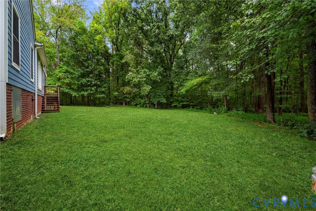 2654 Academy Road, Powhatan, VA 23139 Expansive backyard featuring a level lawn, mature trees, brick and lap siding exterior, and a wooden deck. Virtually edited grass