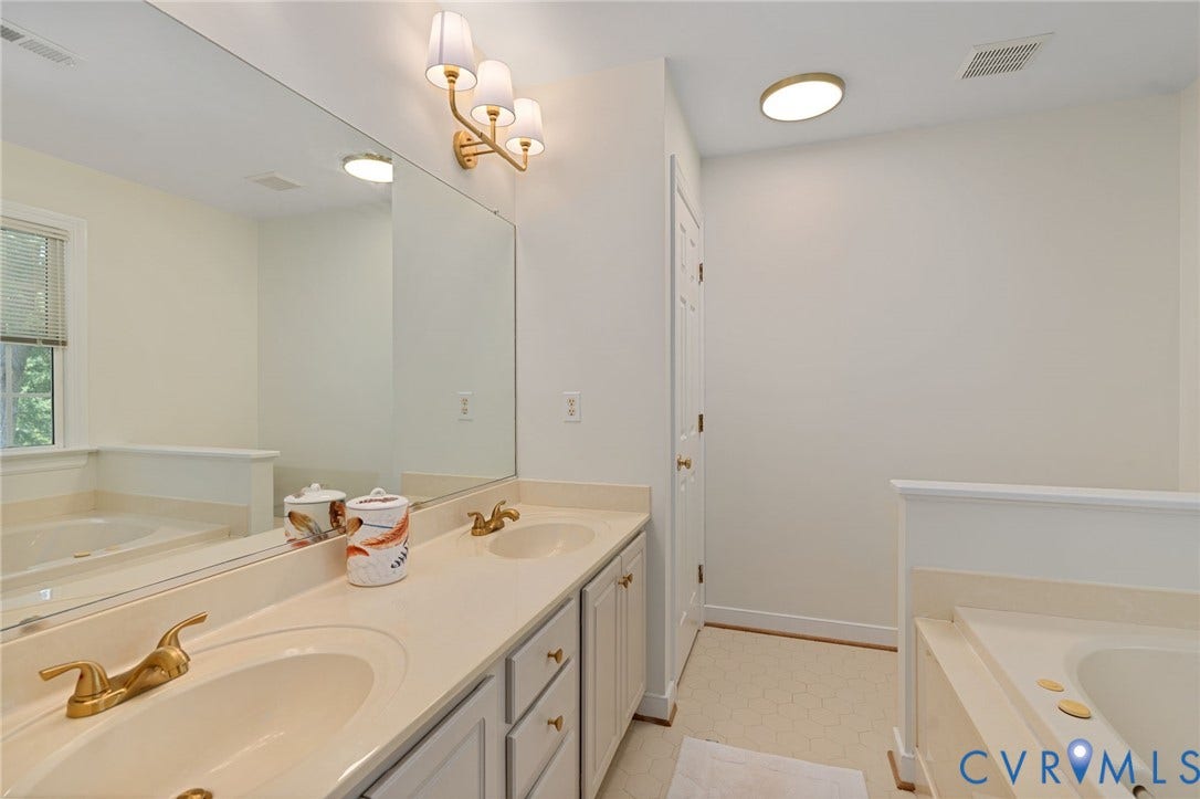 4427 Tweedsmuir Court, Midlothian, VA 23120 Dual-sink vanity with a solid-surface countertop, gold-tone fixtures, oversized wall-to-wall mirror, and a built-in soaking tub