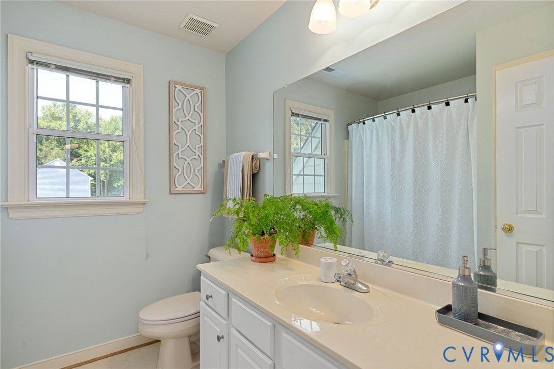 4427 Tweedsmuir Court, Midlothian, VA 23120 Bathroom featuring a white vanity cabinet, solid-surface countertop with an integrated basin, expansive wall-to-wall mirror, multi-pane window with wood trim, and a shower-tub combination