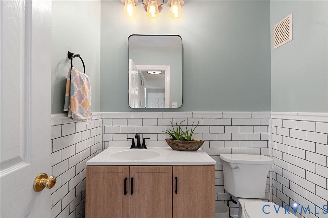 4427 Tweedsmuir Court, Midlothian, VA 23120 Half-wall white subway tile wainscoting, wood-finish vanity with a white countertop, rectangular mirror with rounded corners, and matte black plumbing fixtures