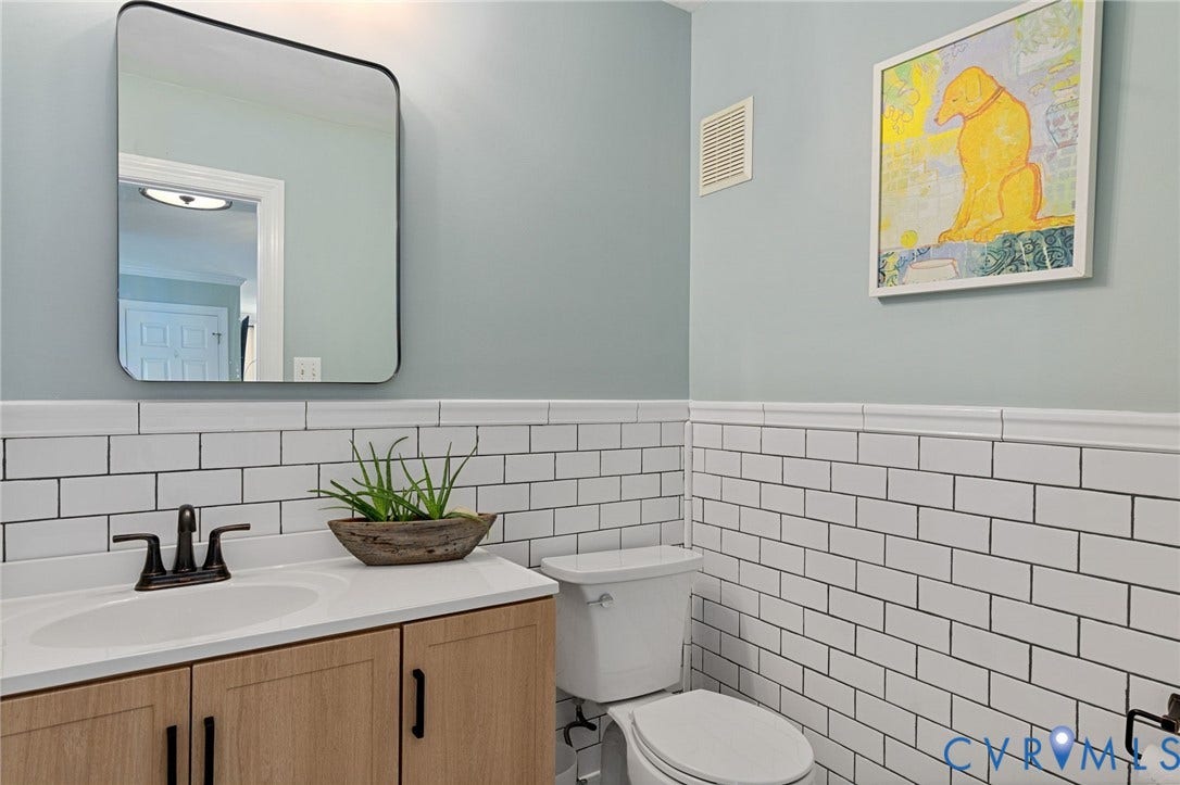 4427 Tweedsmuir Court, Midlothian, VA 23120 Wood-finish vanity cabinet with a white countertop, undermount sink, matte black faucet, and white subway tile wainscoting topped with a rectangular wall-mounted mirror