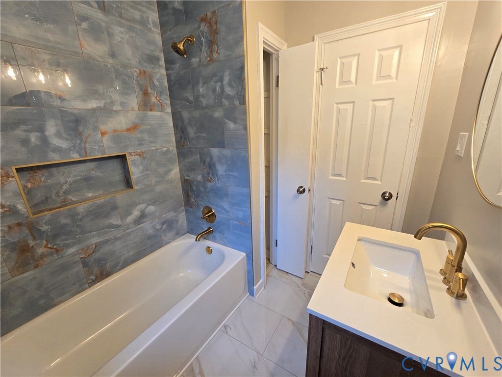 1108 Pierpont Road, Richmond, VA 23225 Bathroom featuring a deep soaking tub with blue-toned tile surround, integrated shower niche, gold-toned plumbing fixtures, and a vanity with a white countertop