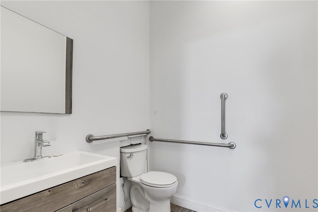 3300 Hull Street, Richmond, VA 23224 Wall-mounted vanity with a rectangular sink, wood-finish cabinetry, frameless mirror, and integrated brushed metal safety grab bars