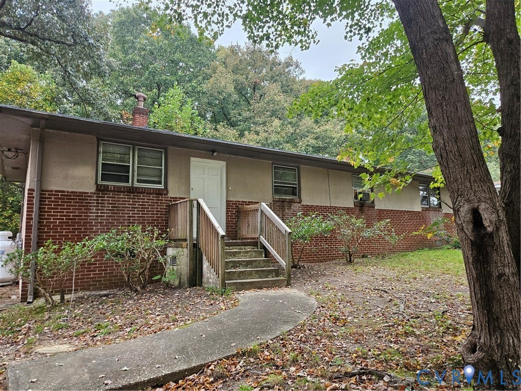 Single-story exterior featuring a brick and stucco facade, a brick chimney, and a concrete pathway leading to a wooden staircase with railing