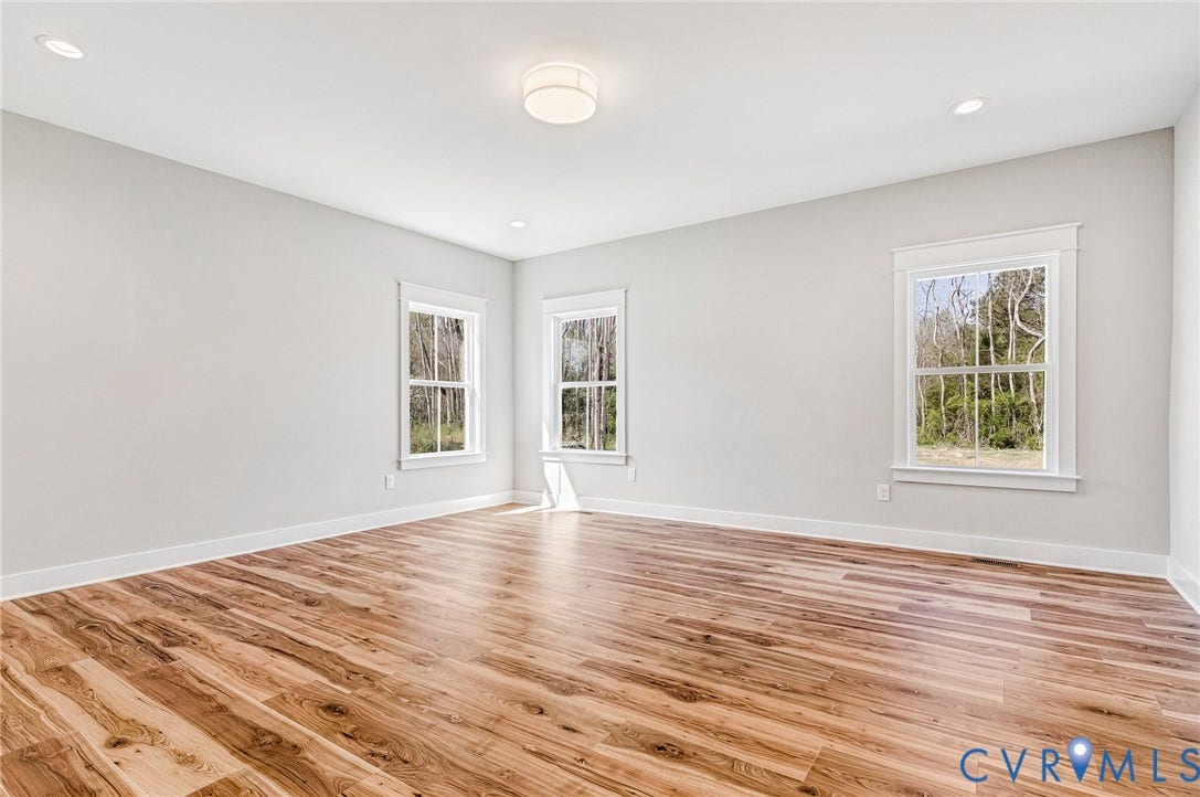 8860 Emily Jane Place, Quinton, VA 23141 This bright room features wide plank wood flooring, light grey walls, white trim, and three windows that provide views of trees
