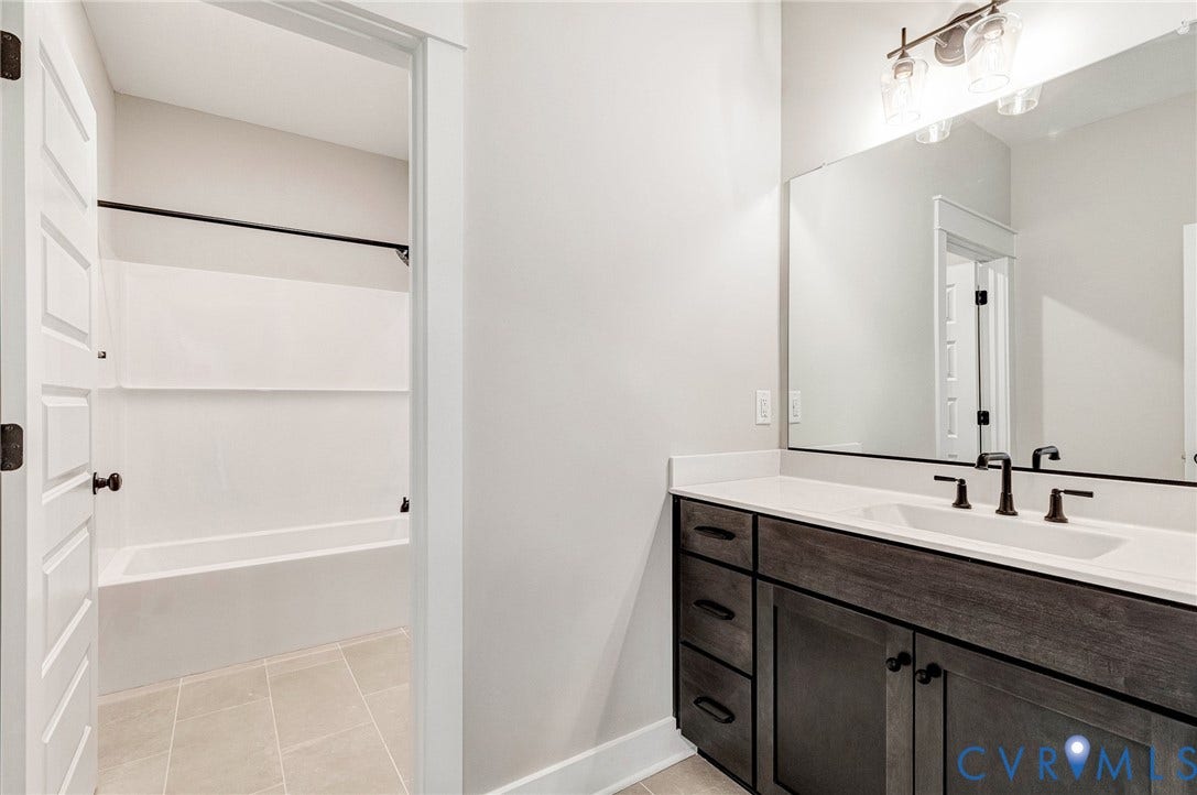 8860 Emily Jane Place, Quinton, VA 23141 The bathroom features a vanity with a white countertop and a rectangular sink, complemented by a large mirror and modern light fixture
