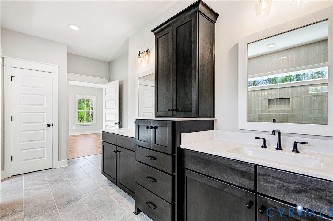 8860 Emily Jane Place, Quinton, VA 23141 This bathroom features dual vanities with dark cabinetry and white countertops, a large framed mirror, and tiled flooring