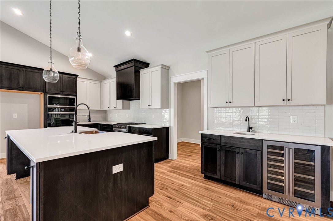 8860 Emily Jane Place, Quinton, VA 23141 The kitchen features an expansive island with a white countertop and a sink with a matte black faucet, hardwood flooring, two-tone cabinetry, and a subway tile backsplash