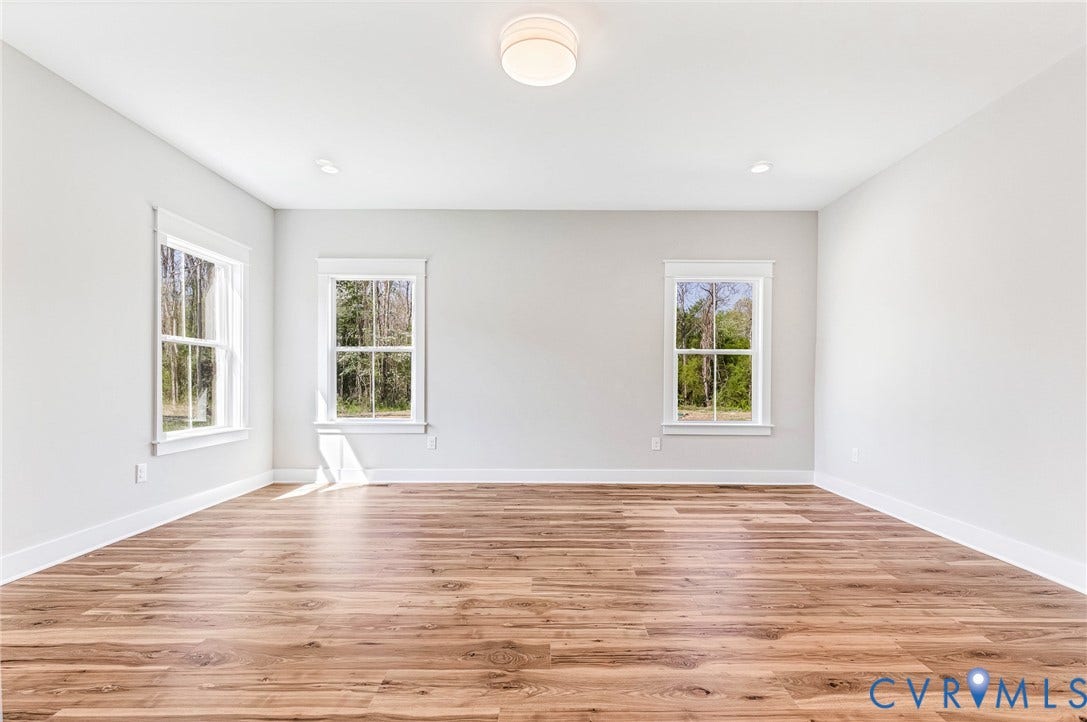 8860 Emily Jane Place, Quinton, VA 23141 An expansive room featuring light-toned walls, rich wooden flooring, and three windows that provide views of natural greenery