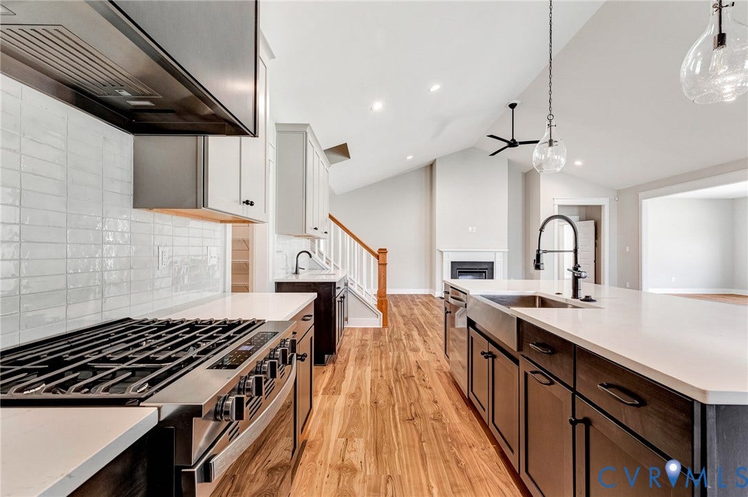 8860 Emily Jane Place, Quinton, VA 23141 The kitchen features a large island with a stainless steel sink and a contemporary black faucet, a white tiled backsplash, and a stainless steel oven with a range hood