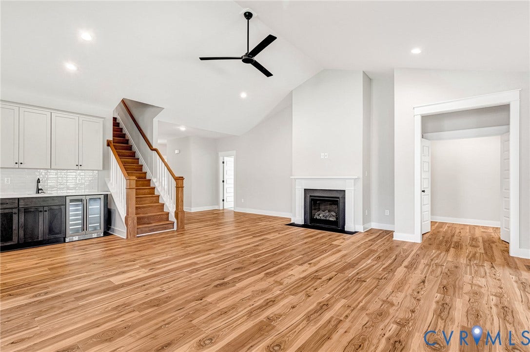 8860 Emily Jane Place, Quinton, VA 23141 Expansive room featuring light wood flooring, a fireplace with a white mantel, and a beverage station with white upper cabinets and a tiled backsplash