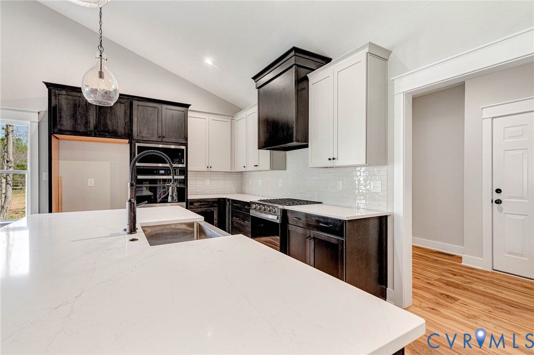 8860 Emily Jane Place, Quinton, VA 23141 Modern kitchen with a spacious island featuring a sink and a contemporary faucet, white countertops, a gas range, and two-tone cabinetry with black and white finishes