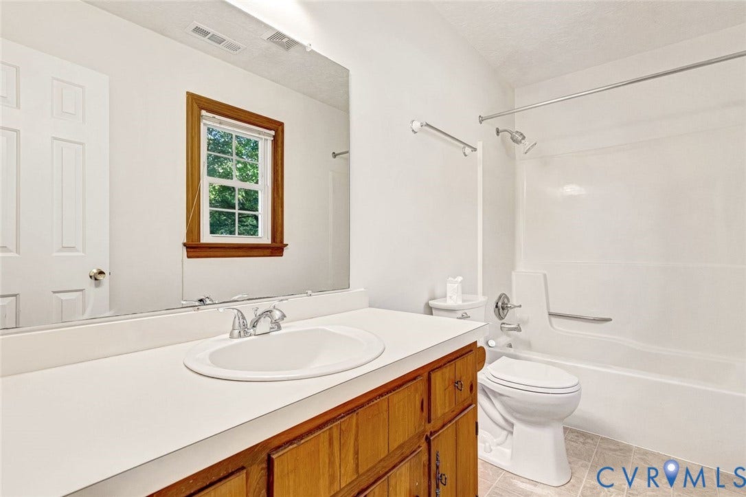 6432 Bellflower Circle, Mechicsville, Mechanicsville, VA 23111 Bathroom featuring a wood-finish vanity with a white countertop and oval undermount sink, large wall-mounted mirror, combination tub and shower with a chrome fixture, and a window with wood trim