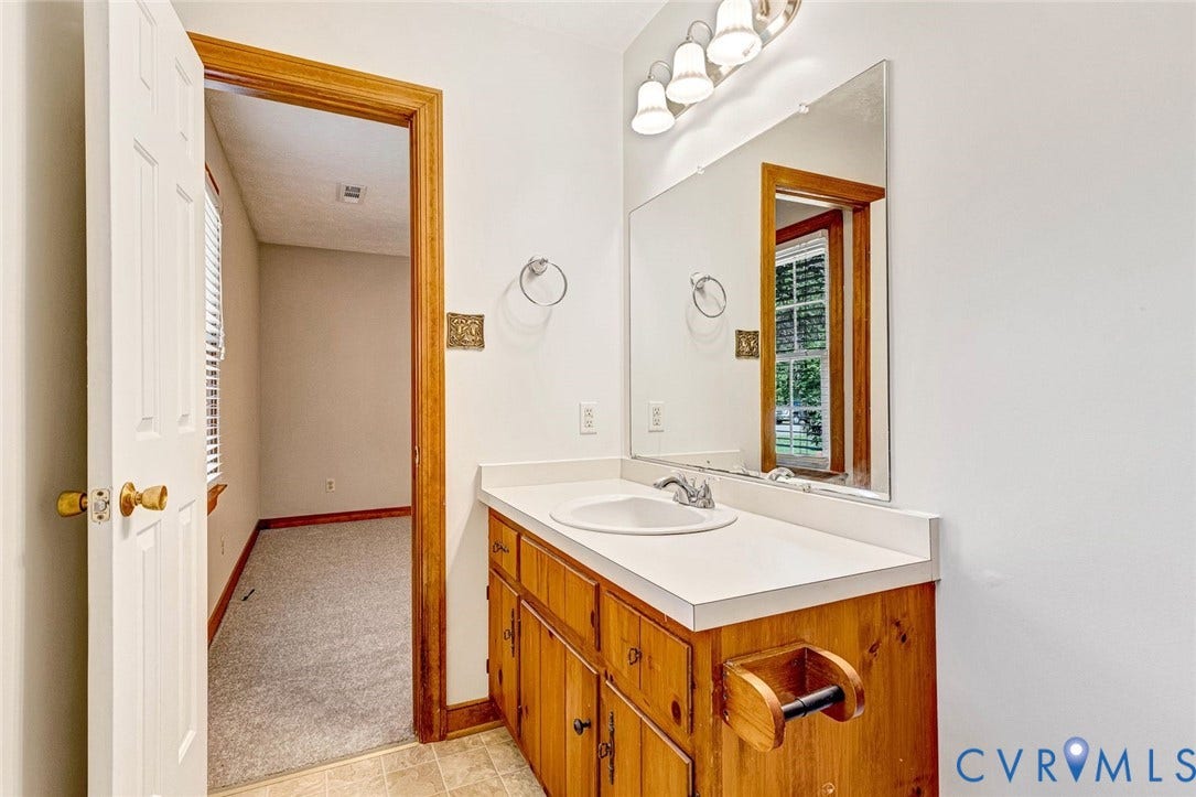 6432 Bellflower Circle, Mechicsville, Mechanicsville, VA 23111 Vanity featuring wood cabinetry, a solid-surface countertop with an integrated basin, a large wall-mounted mirror, and a three-light fixture