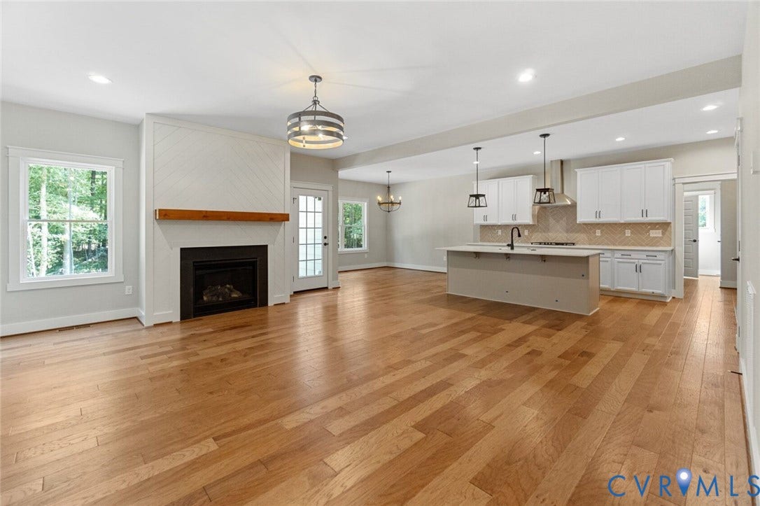 14270 Tower Road, Scotchtown Estates, Montpelier, VA 23047 Open concept area featuring wood-finish flooring, a fireplace with a wood mantel and herringbone tile surround, white shaker-style cabinetry, an expansive kitchen island with a built-in sink, and custom pendant lighting