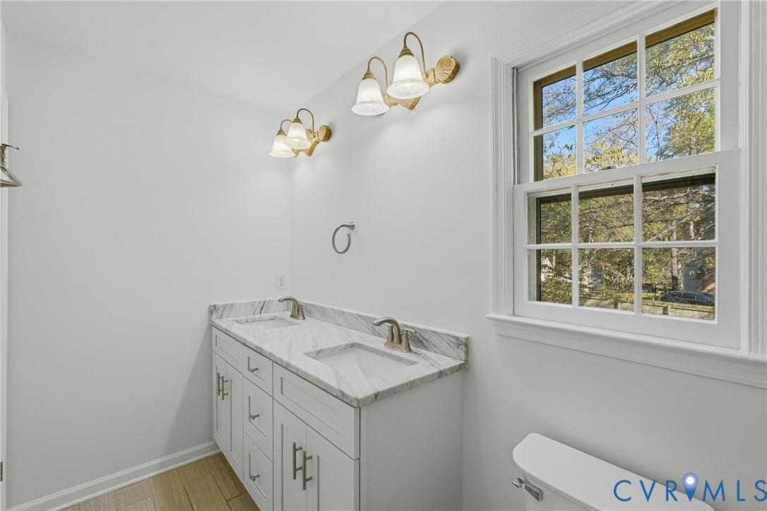 12506 Mandolin Drive, Chesterfield, VA 23113 Dual-sink vanity with a stone-top counter, undermount rectangular basins, brushed metal faucets, multi-light wall fixtures, and multi-pane window