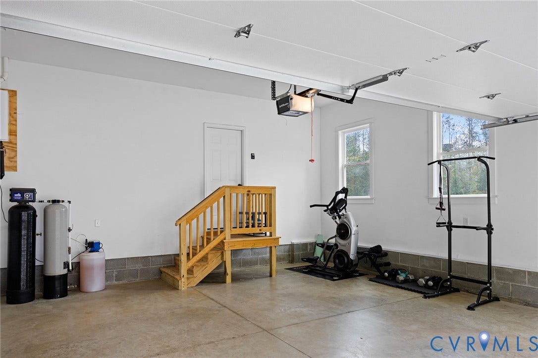 360 Anderson Mill Drive, Anderson Mill, Bumpass, VA 23024 Garage space featuring concrete flooring, painted masonry walls, dual windows, and an integrated water filtration system with a wooden staircase access point