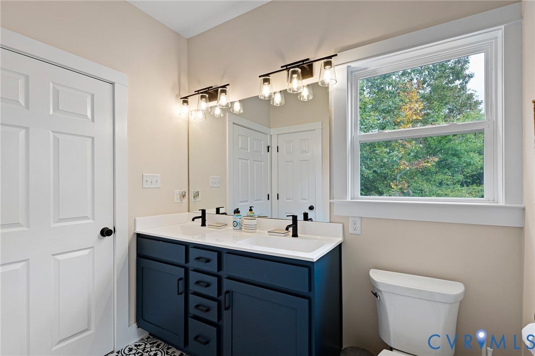 360 Anderson Mill Drive, Anderson Mill, Bumpass, VA 23024 Dark blue dual-sink vanity with a white countertop, two matte black faucets, oversized wall mirror, and two multi-light fixtures