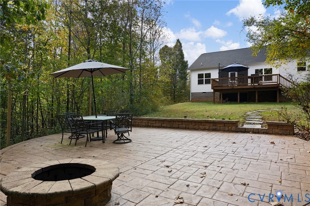 360 Anderson Mill Drive, Anderson Mill, Bumpass, VA 23024 Stamped concrete patio featuring a built-in stone fire pit, tiered retaining wall, raised wooden deck, and a natural woodland backdrop