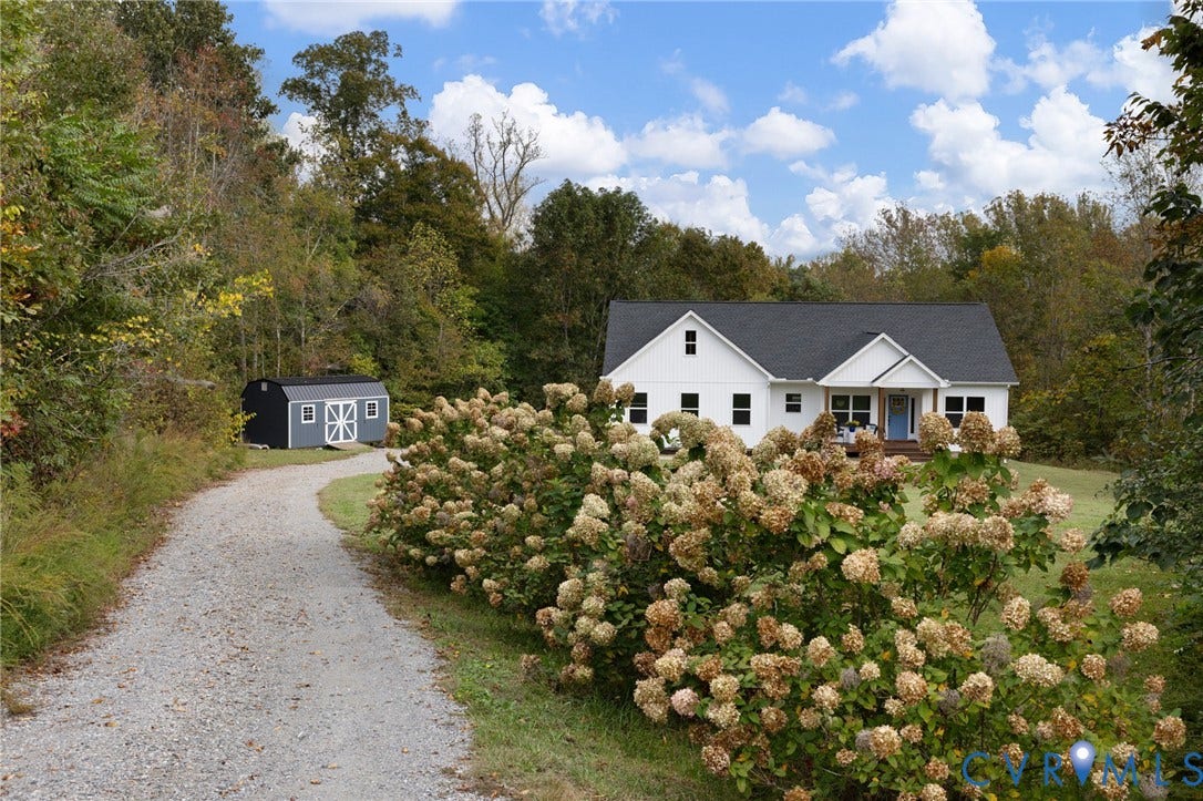 360 Anderson Mill Drive, Anderson Mill, Bumpass, VA 23024 Single-story exterior featuring white board and batten siding, a dark shingled roof, a graveled driveway, and a detached storage structure surrounded by wooded landscape
