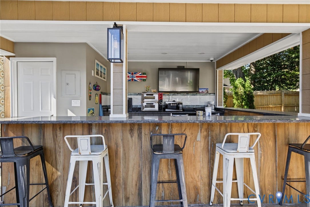 4504 Argonne Court, Glen Allen, VA 23060 Covered outdoor kitchen featuring a stone-topped bar counter, wood-finish paneling, and an integrated exterior lantern-style lighting fixture