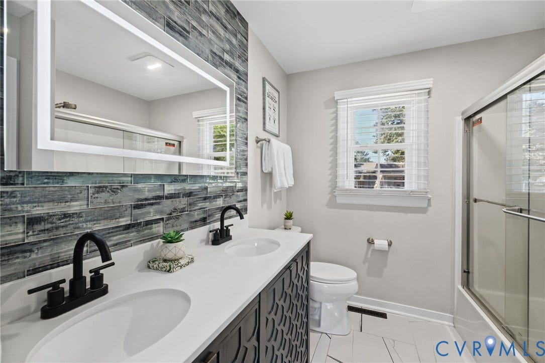 4504 Argonne Court, Glen Allen, VA 23060 Double vanity with white solid-surface countertop and matte black faucets, textured charcoal-finish cabinet cabinetry, rectangular LED-backlit mirror, blue-toned glass tile backsplash, and walk-in shower with sliding glass enclosure