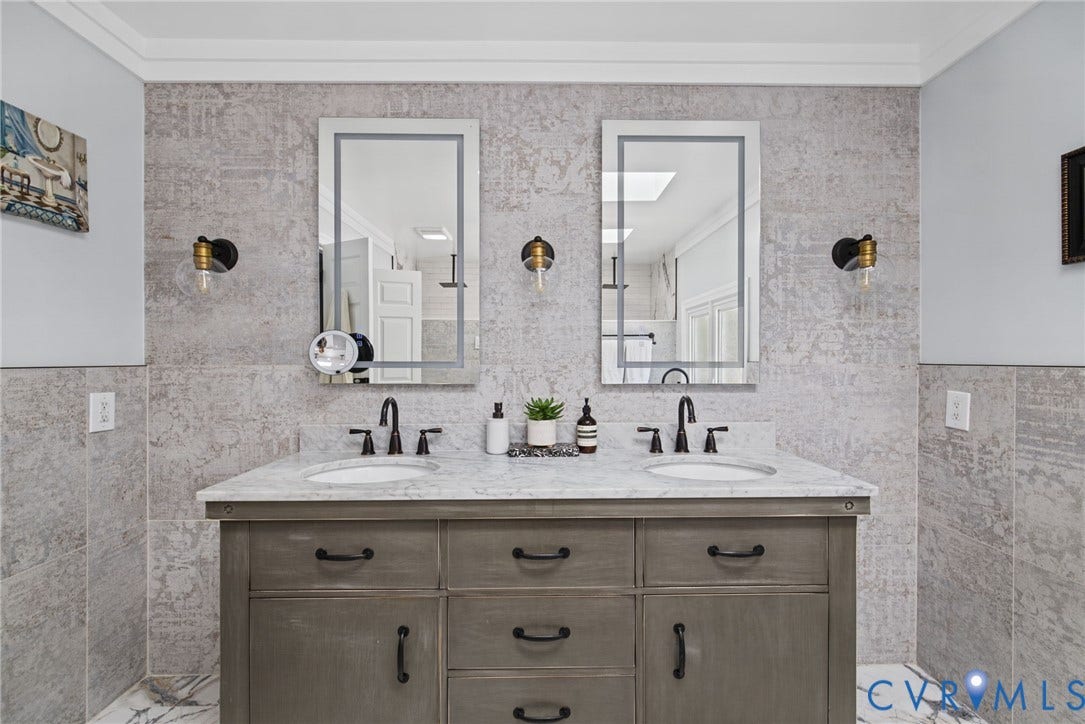 4504 Argonne Court, Glen Allen, VA 23060 Dual-sink vanity with stone countertop, matte black fixtures, framed vanity mirrors, and wall-mounted light sconces set against full-height textured tile wall cladding