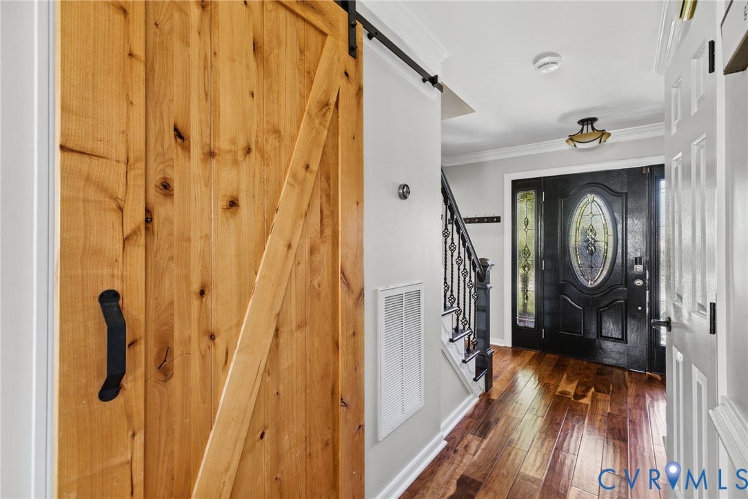 4504 Argonne Court, Glen Allen, VA 23060 Entryway featuring wood-finish flooring, a natural wood sliding barn door with matte black hardware, and an exterior door with decorative leaded glass inserts, complemented by a staircase with decorative wrought iron balusters and crown molding