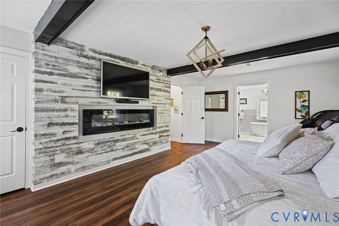 4504 Argonne Court, Glen Allen, VA 23060 Weathered wood-finish accent wall with a built-in linear electric fireplace, exposed black structural beam, wood-finish flooring, and geometric metal-frame chandelier
