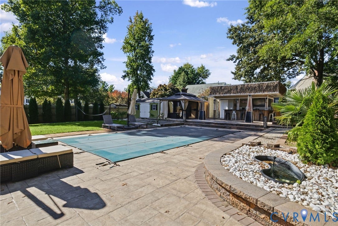 4504 Argonne Court, Glen Allen, VA 23060 Outdoor living space featuring an in-ground swimming pool, stone paver patio, custom bar structure with thatched roofing, integrated water feature, and a hardscaped retaining wall