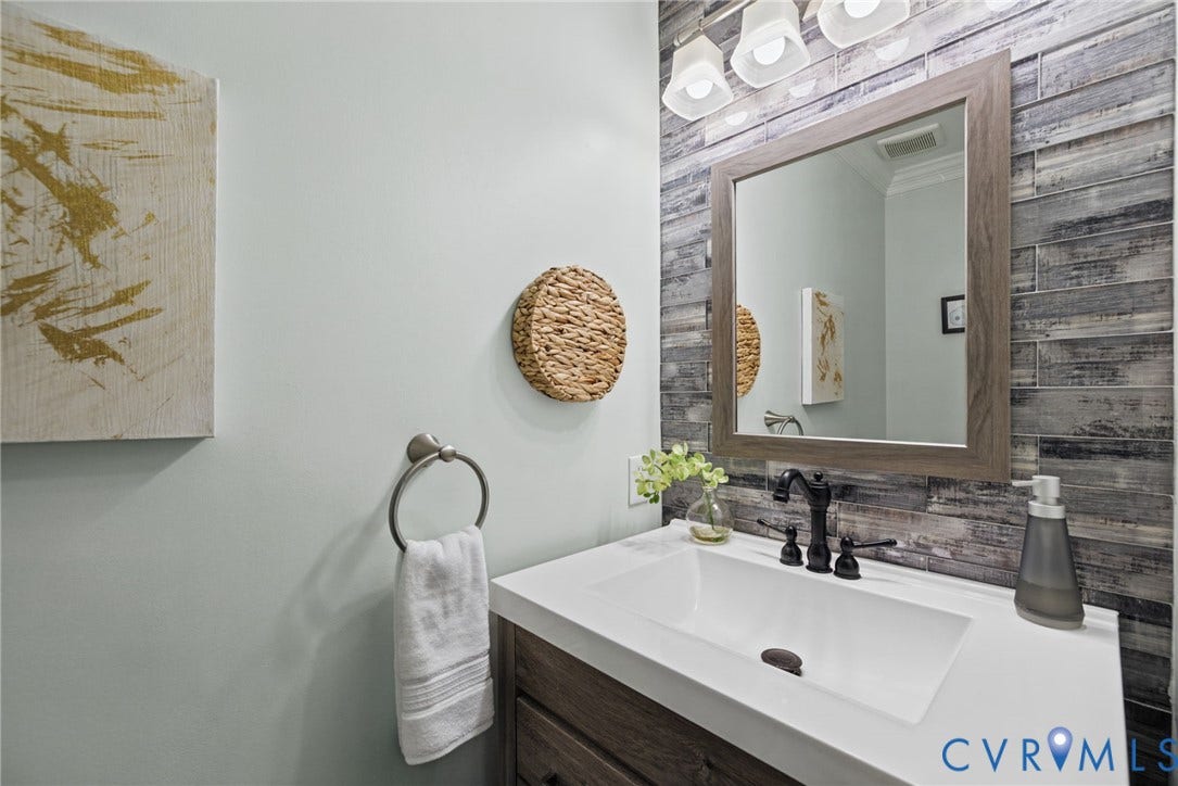 4504 Argonne Court, Glen Allen, VA 23060 Vanity featuring a white countertop, undermount sink, dark-finish widespread faucet, and wood-finish cabinetry, accented by horizontal tile wall cladding, a framed mirror, and a multi-bulb light fixture
