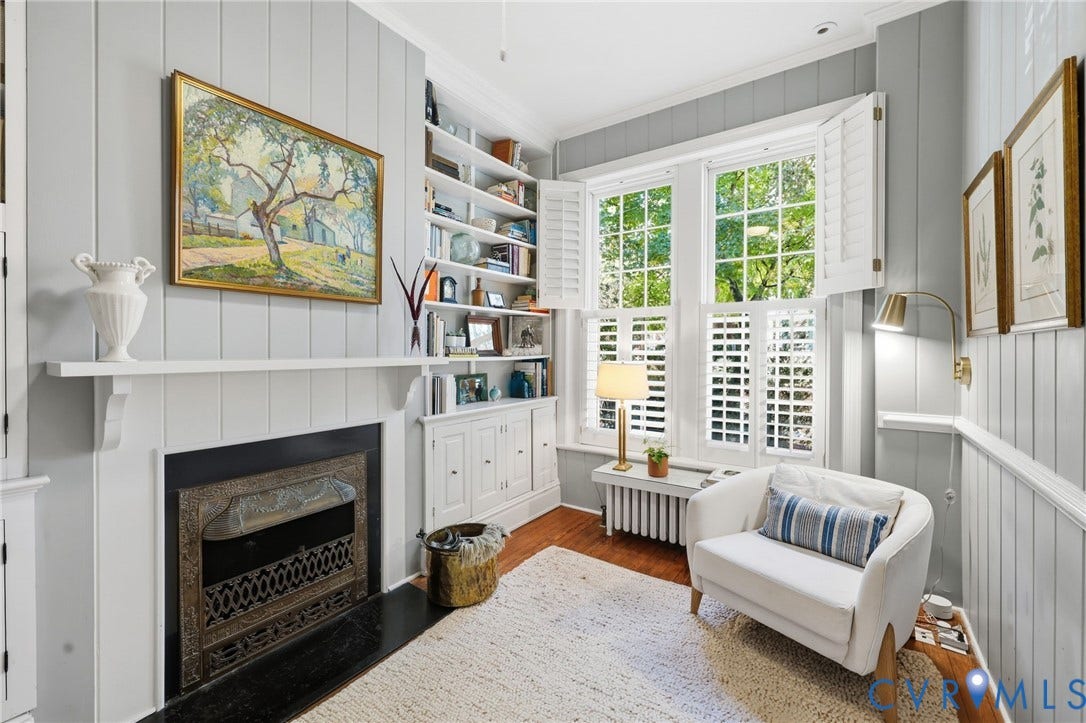 107 N Harvie Street, The Fan, Richmond, VA 23220 Fireplace with a decorative metal surround and hearth, vertical wood paneling, built-in floor-to-ceiling shelving, and windows featuring plantation shutters