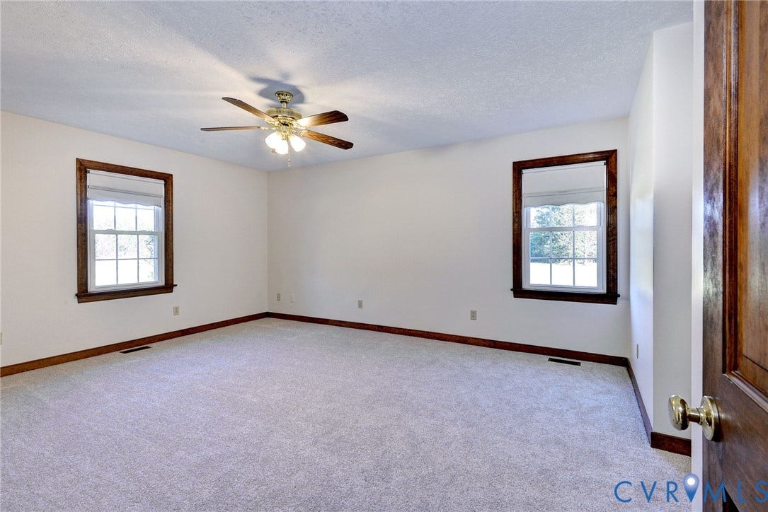 14151 Black Horse Lane, Lanexa, VA 23089 Neutral-toned carpeting, dual windows with wood-finish trim, and a multi-blade ceiling fan with integrated light fixture