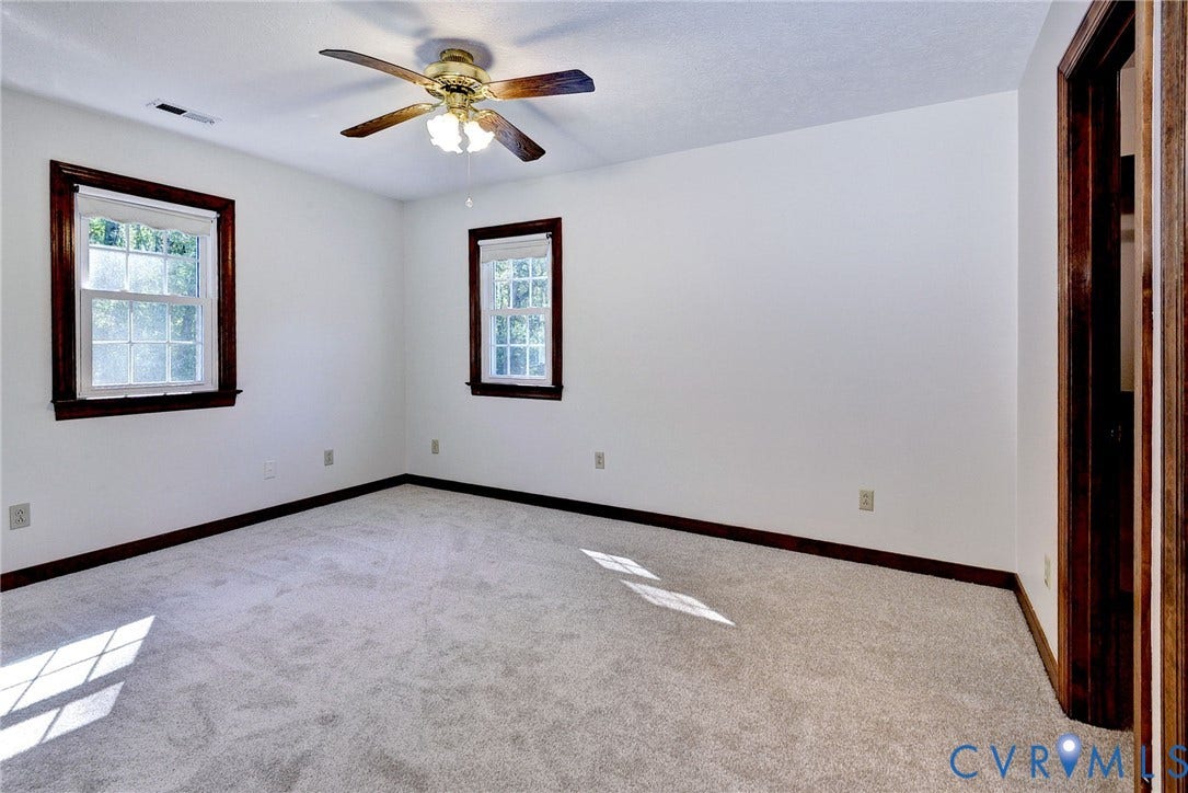 14151 Black Horse Lane, Lanexa, VA 23089 Room featuring neutral carpeting, dark wood-finish window trim, and a ceiling fan with integrated light fixture