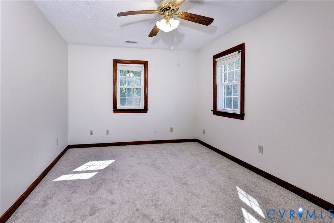 14151 Black Horse Lane, Lanexa, VA 23089 Neutral-toned interior room featuring wall-to-wall carpeting, two double-hung windows with dark wood-finish trim, and a ceiling fan with integrated lighting