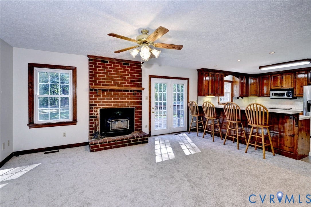 14151 Black Horse Lane, Lanexa, VA 23089 Red brick fireplace with a wood-finish mantel and inset stove, wood cabinetry, glass-paneled double doors, and a ceiling fan with integrated lighting