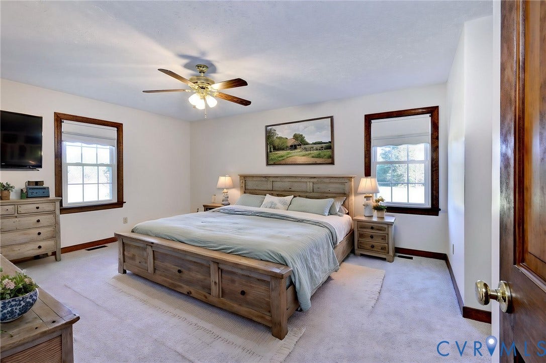 14151 Black Horse Lane, Lanexa, VA 23089 VIRTUAL STAGING - Neutral-toned room featuring double-pane windows with dark wood trim, a ceiling fan with integrated lighting, and a six-panel wood door with brass-finish hardware