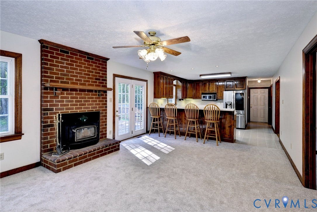 14151 Black Horse Lane, Lanexa, VA 23089 Floor-to-ceiling brick fireplace with a wood-finish mantel and inset stove, wood cabinetry, breakfast bar, and glass-paned double doors