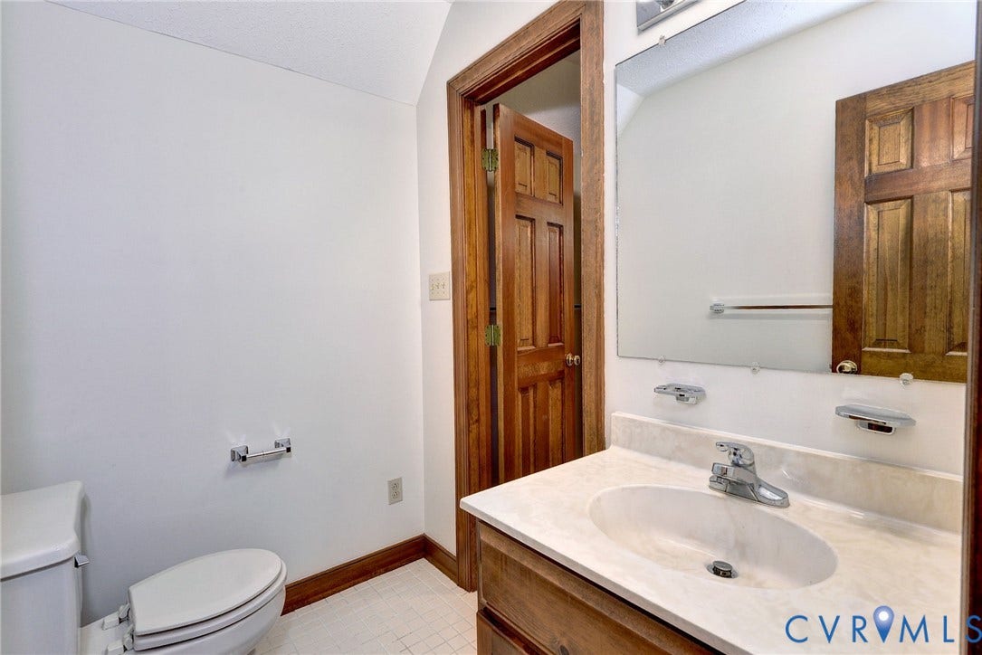 14151 Black Horse Lane, Lanexa, VA 23089 Vanity featuring a light-toned countertop with an integrated basin, wood-finish cabinetry, a large wall-mounted mirror, ceramic tile flooring, and solid wood interior door with matching trim